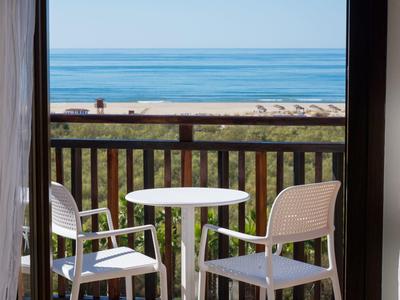 Balcón con mesa y sillas blancas con vista a la playa y el mar en clima despejado.