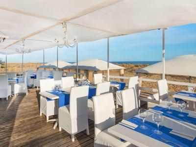 Restaurante al aire libre con techo, suelo de madera y vista al mar en cielo despejado.