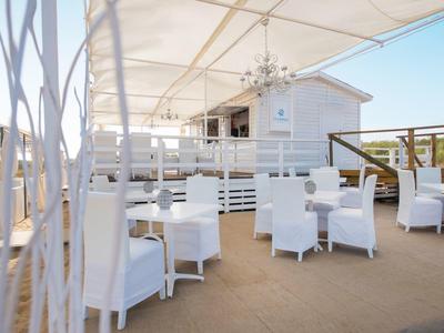 Terraza con mesas y sillas blancas bajo un toldo de tela, cielo despejado al fondo.