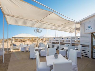Terraza al aire libre con mesas y sillas blancas bajo toldos, con vista a un paisaje desértico.