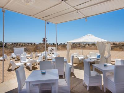 Área al aire libre con sillas y mesas blancas bajo carpas en un paisaje seco y soleado.