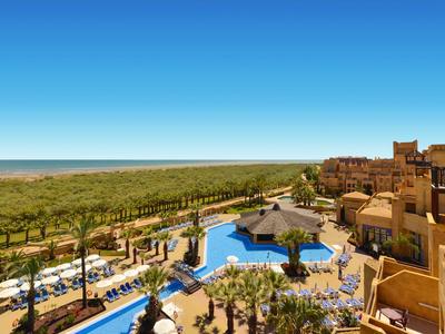 Luxusní hotel s velkým bazénem, palmami a výhledem na moře za jasné oblohy.