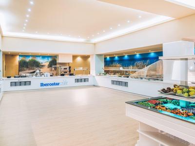 Lobby de hotel moderna y luminosa con recepción, buffet de frutas y murales panorámicos.