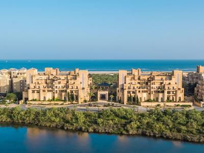 Vista de una ciudad costera con edificios beige, rodeada de agua y vegetación verde.