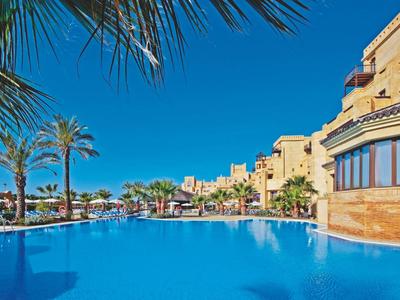 Venkovní prostor hotelu s několika stoly a židlemi, rostlinami a dekorativní architekturou.