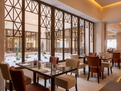 Vista interior de un restaurante de hotel con decoración moderna y grandes ventanales al patio.