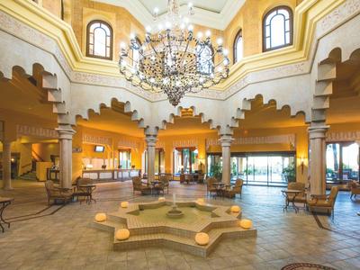 Un amplio vestíbulo de hotel luminoso con fuente de mosaico y candelabro de estilo oriental.