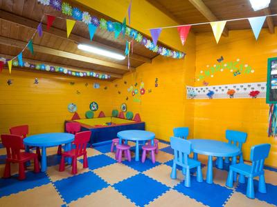 Sala de juegos colorida para niños con mesas y sillas pequeñas, decoración en la pared y banderines.
