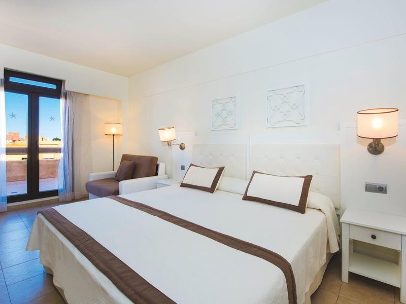 Habitación de hotel luminosa con cama doble, sofá y ventana de balcón con vista al exterior.