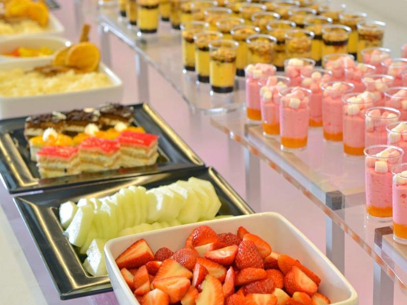 Bufé con frutas frescas y postres en pequeños vasos dispuestos en una fila sobre la mesa.