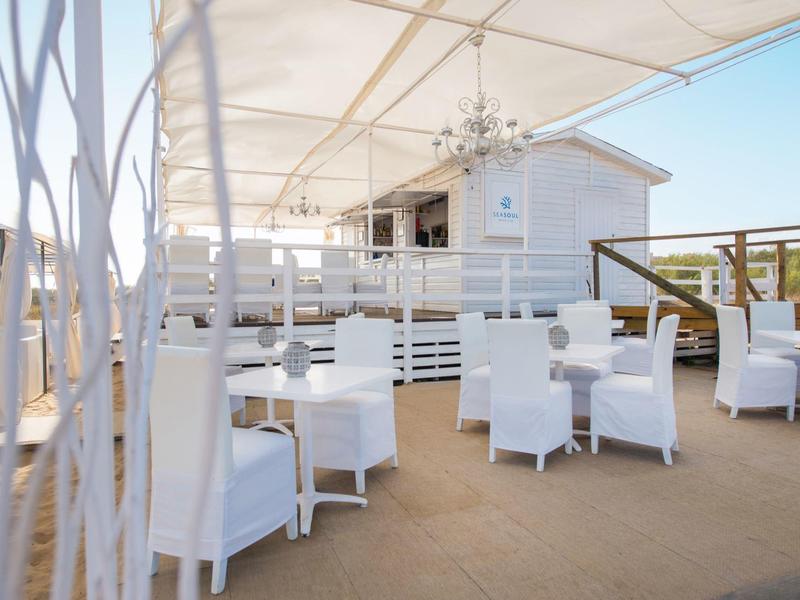 Terraza con mesas y sillas blancas bajo un toldo de tela, cielo despejado al fondo.
