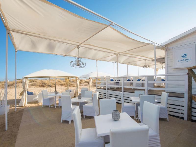 Terraza al aire libre con mesas y sillas blancas bajo toldos, con vista a un paisaje desértico.