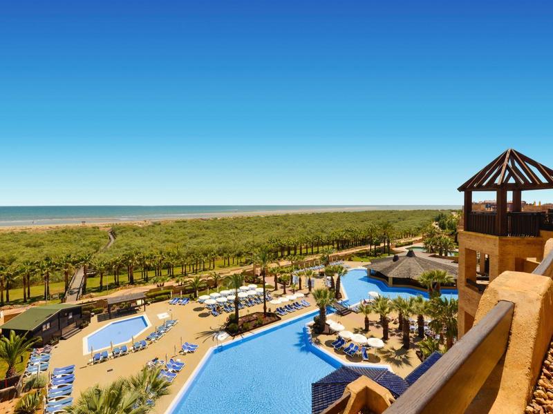 Vista de un hotel con piscinas, tumbonas y mar de fondo bajo un cielo despejado.