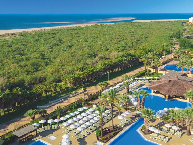 Gran complejo hotelero con grandes piscinas, tumbonas y vista a la playa y el mar al fondo.