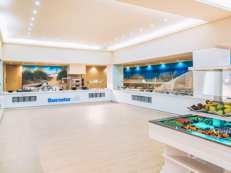 Lobby de hotel moderna y luminosa con recepción, buffet de frutas y murales panorámicos.