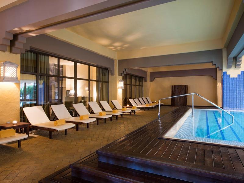 Área interior con piscina, tumbonas y elementos de pared modernos con luz cálida.