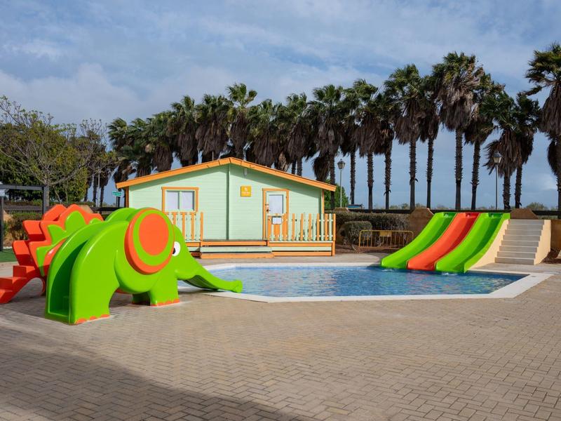 Piscina con toboganes coloridos y palmeras en un área recreativa al aire libre.