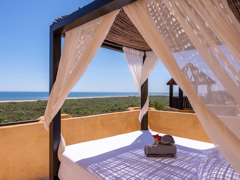 Cama al aire libre con cortinas blancas y vista al mar bajo un cielo azul despejado.