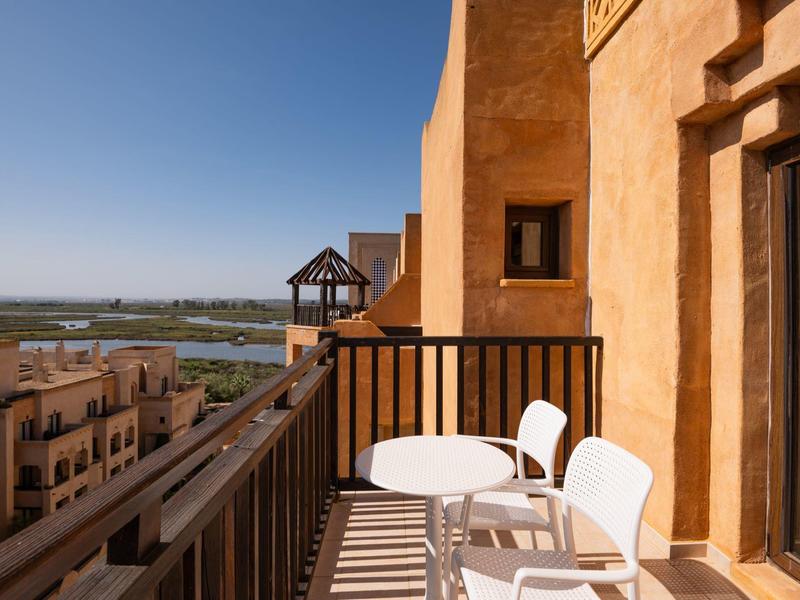 Balcón con sillas blancas y mesa, vistas a edificios y paisaje bajo cielo despejado.
