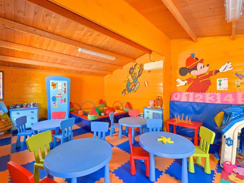 Sala de juegos infantil colorida con mesas azules y sillas de colores bajo techo de madera.