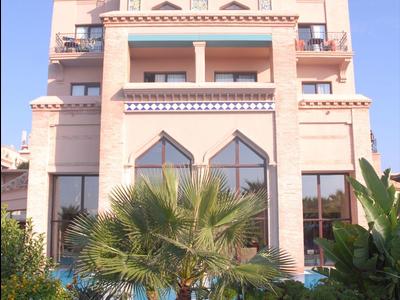 Hôtel à plusieurs étages avec terrasses et jacuzzi dans un jardin verdoyant sous un ciel bleu.