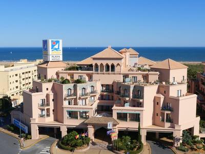 Grand bâtiment hôtelier près de la mer avec façades roses et ciel bleu en arrière-plan.