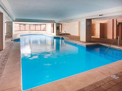 Piscine intérieure avec eau claire bleue et carrelage beige, entourée de murs en bois.