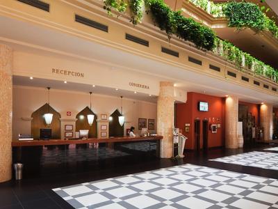 Hall d'hôtel avec réception en bois foncé et balcons verts au-dessus