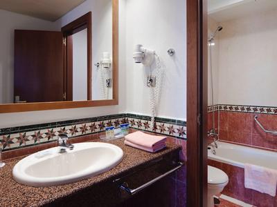 Salle de bain moderne avec lavabo, grand miroir et baignoire avec serviettes.