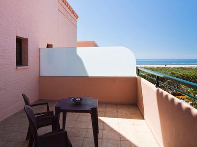Balcon avec deux chaises, une table et un pare-vue avec vue sur la mer par jour ensoleillé.