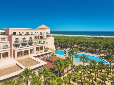 Luxe hotel met zwembaden en palmbomen onder een blauwe lucht en zee op de achtergrond.