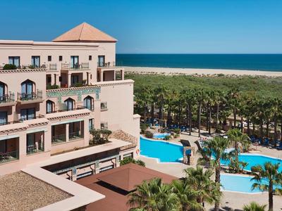 Hôtel avec grandes piscines, palmiers et vue sur la mer par temps ensoleillé.