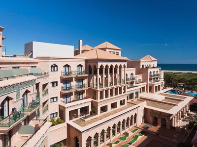 Groot hotelgebouw in mediterrane stijl met uitzicht op zee en blauwe lucht.