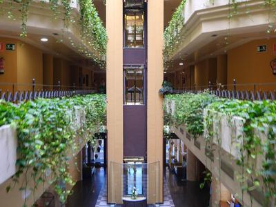 Cour intérieure d'un hôtel à deux étages avec plantes et ascenseur au centre