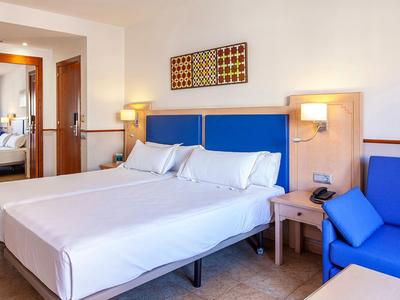 Chambre d'hôtel lumineuse avec deux lits simples, têtes de lit bleues et décor moderne.