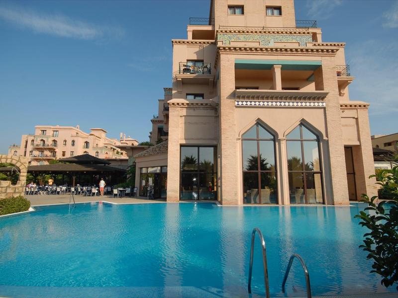 Grand bâtiment d'hôtel avec une impressionnante piscine sous un ciel dégagé.