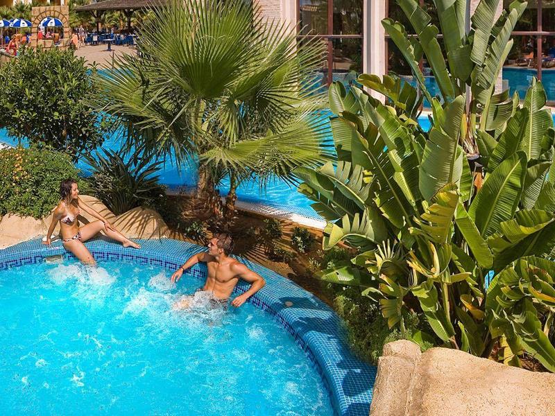 Deux personnes se détendent dans une petite piscine avec des palmiers et des rochers dans un hôtel.