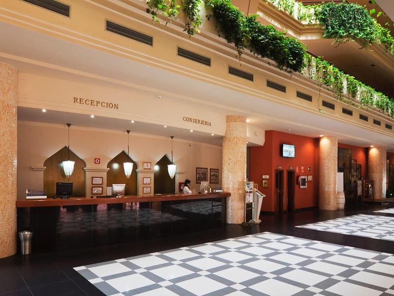 Hall d'hôtel avec réception en bois foncé et balcons verts au-dessus