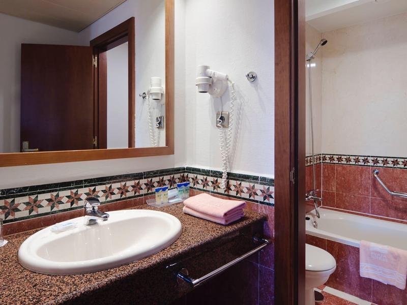 Salle de bain moderne avec lavabo, grand miroir et baignoire avec serviettes.