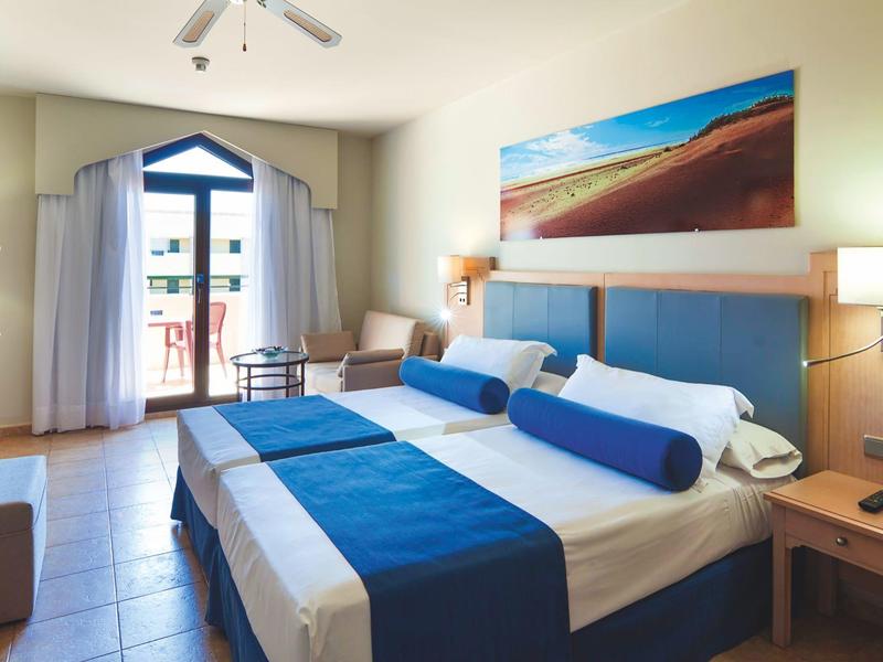 Chambre d'hôtel moderne avec lit double, accents bleus et accès au balcon.