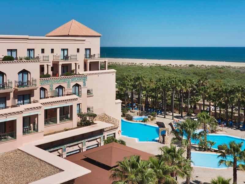 Hôtel avec grandes piscines, palmiers et vue sur la mer par temps ensoleillé.