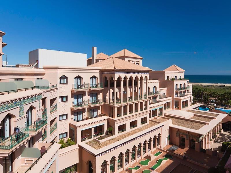 Grand bâtiment d'hôtel avec balcon et vue sur la mer sous un ciel bleu clair.