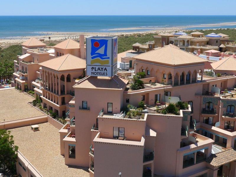 Grand hôtel avec terrasses près de la plage et de la mer sous un ciel clair.