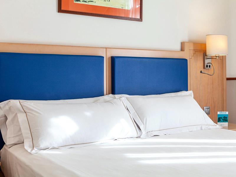 Chambre d'hôtel lumineuse avec lit double et têtes de lit rembourrées bleues.