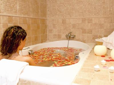 Eine Frau entspannt in einer mit Rosenblättern gefüllten Badewanne in einem hellen Badezimmer.