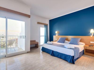 Helles Schlafzimmer mit großem Doppelbett, blauer Akzentwand und Balkon mit Tisch und Stühlen.