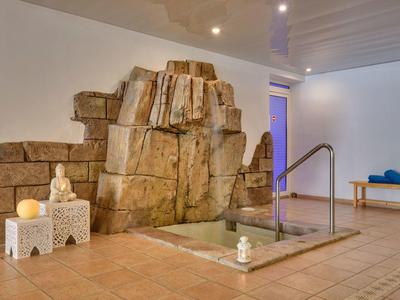 Innenraum mit kleinem Wellnesspool, künstlichem Felsen, Kerzen und einfacher Holzbank.