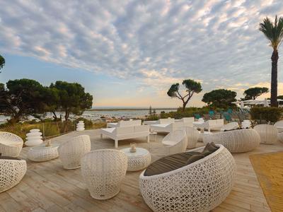 Offener Terrassenbereich mit weißem Rattanmöbel, Palmen und Blick auf das Meer bei Sonnenuntergang.