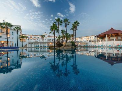 Großer Hotelpool mit Palmen und mehrstöckigen Gebäuden bei klarem Himmel am Abend.