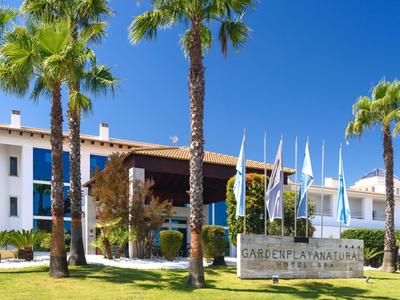 Hotel building with palm trees and flower-filled green areas under clear blue sky
